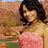 A pixelated image of a person with dark curly hair wearing a pink polka-dot top, standing against an outdoor background.