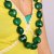 A pixelated necklace with dark green and teal beads on a yellow background, held by hands.