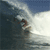 Animated contact sheet showing three sequential frames of a surfer riding a large ocean wave under a blue sky.