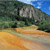 Pixelated landscape with rocky hill, green foliage, and blue sky above a sandy foreground.