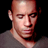 Static pixelated image of a bald man's face and upper shoulders against black background, wearing gray shirt with visible neck and jawline details.
