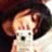 Pixelated image of a person with light brown hair wearing a white top, set against dark background.