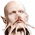 Pixelated image of a bald figure with pointed ears, closed eyes, and a mustache, wearing a dark suit jacket over a light shirt.