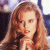 A static pixelated image shows a person with long light brown hair, fair skin, and a neutral expression, with a blurred background of indistinct shapes and colors.