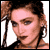 Pixelated static image of a person with brown hair tied back, wearing hoop earrings and dark clothing against a white background.