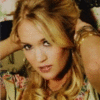 A static image of a person with light brown hair styled in loose waves, wearing a floral-patterned top with visible pink and green colors.