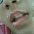 A person's face with a small white dot on the cheek, wearing a pink garment, shown in three with mouth opening and closing
