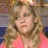 A pixelated close-up of a person with light brown curly hair wearing a pink top against a blurred background with brown and blue tones.