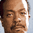 A pixelated promotional graphic with red text on black background, featuring a partial portrait of a man and broadcast details.