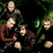 Group of people in dark clothing with green foliage background, some in red shirts, positioned in a dense arrangement with visible hands and arms.