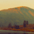 A pixelated landscape with a hazy sky transitioning from pale yellow to orange, featuring indistinct shapes resembling buildings or structures in muted brown and gray tones against a blurred background.