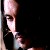 Pixelated still image of a figure in dark clothing holding a light-colored object against a black background.