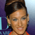 Pixelated close-up of a person with dark hair styled up, wearing an orange garment and earrings, against a blue-purple gradient background with partial text.