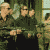 Animated sequence showing a group of people in dark clothing holding rifles in front of a building with green and windows