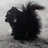 Pixelated black shape with rounded edges and two light circular spots on a gray background, appearing as an abstract or obscured figure.