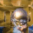 Pixelated static image of a person with light-colored hair wearing glasses and a dark jacket over a light shirt, set against a warm-toned background.