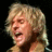 Pixelated close-up of a person with light brown hair, mouth open in mid-expression against dark background.