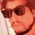 A pixelated close-up of a person wearing dark sunglasses and a white shirt, with a blurred background.