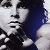 Black-and-white close-up of a person with dark curly hair holding a microphone, set against a blue background.
