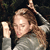A pixelated figure with light brown hair wears a gray top and holds a white object near their face against a dark background.