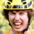 Pixelated image of a person wearing a yellow helmet with blue and black accents, smiling broadly with eyes closed against a blurred green-yellow background.