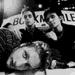 Black-and-white image of four people in two distinct poses with partial text elements visible in the background.