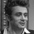 Black-and-white image of a person with curly hair in three distinct poses: smiling left, serious front-facing, and neutral side profile.