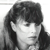 Pixelated grayscale portrait of a person with shoulder-length dark hair, side-swept bangs, and a neutral expression against a plain background.