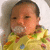 A baby in a yellow patterned outfit with white collar, positioned against light background.