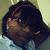 Pixelated image of a person with dark hair and red headband, wearing glasses and light-colored clothing against blurred background.