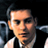 Pixelated static image of a person's face and upper torso in formal attire against dark background with partial shoulder/neck details visible.
