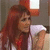 A woman with long red hair in a white top, seated indoors with an orange-framed window behind her.