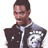 Pixelated static image of a person wearing a dark jacket with white text on the chest, standing against a plain background.