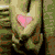 A hand holds a pink heart against green fabric, with cloud-shaped hearts in blue sky and grayscale hands holding an ampersand.