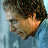 Pixelated image of a person with dark curly hair and light skin, wearing a blue garment against a light blue background.