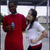 Two people in red and white shirts stand close together, one holding a blue object while the other leans slightly toward them.