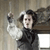 Pixelated figure in dark clothing with raised arm holding a small object against a muted background.