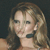 A pixelated close-up of a person with light brown hair, wearing a dark strap over one shoulder against a dark background.