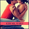 A static image shows two people kissing with arms forming a heart shape, overlaid with a red banner reading 'KISS ME, HARD' in black capital letters.