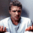 Pixelated static image of a person with short dark hair wearing a white shirt, hands raised in front of the body against a gradient background.