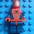 Pixelated Spider-Man figure in red and blue pose against a blue background with repeated 'L' shapes, next to bold text reading SPIDERMAN!