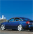 Blue sedan car with silver wheels on a road under clear blue sky, pixelated image with visible compression artifacts.