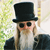 A static image shows a person with long white hair and beard wearing a black top hat and sunglasses, positioned left of a black background with white text fragments.