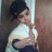 Pixelated static image of a person with dark hair tied up, wearing a white top and dark lower garment, standing against a light vertical structure.