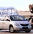 Pixelated static image of a light-colored sedan on a road with a blurred background featuring a bridge and a person standing near the vehicle.