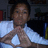 A person in a white shirt forms a heart shape with hands, set against a dark background with blurred objects.