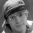 Black-and-white pixelated image of a person wearing a cap with dark hair visible beneath, facing slightly left.