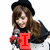 A person with long brown hair and a black beret holds a microphone, wearing a dark jacket over a white shirt. Red text overlays change across frames.
