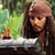 Pixelated image of a person with long dark hair wearing a brown headband, holding a silver sword, standing before a green and brown background with a small fire.