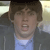 Pixelated close-up of a person with brown hair wearing a dark jacket over a light blue shirt, mouth open in a shout or yell.